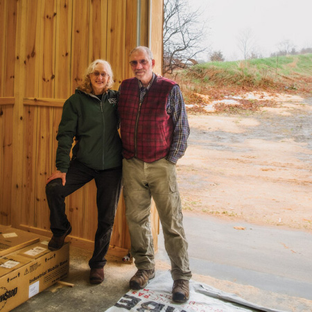 Peg Coleman and Ed Neuhauser stand in the doorway of a workshop on their property in Tompkins County, New York